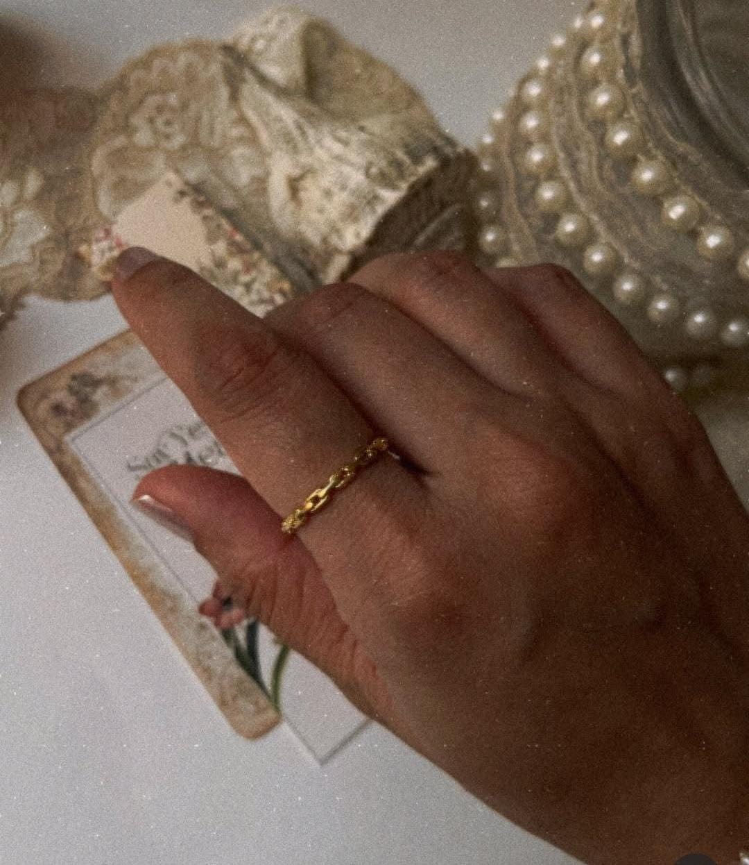 Gold vermeil thin link stack band ring worn on hand with vintage lace and pearls in background.
