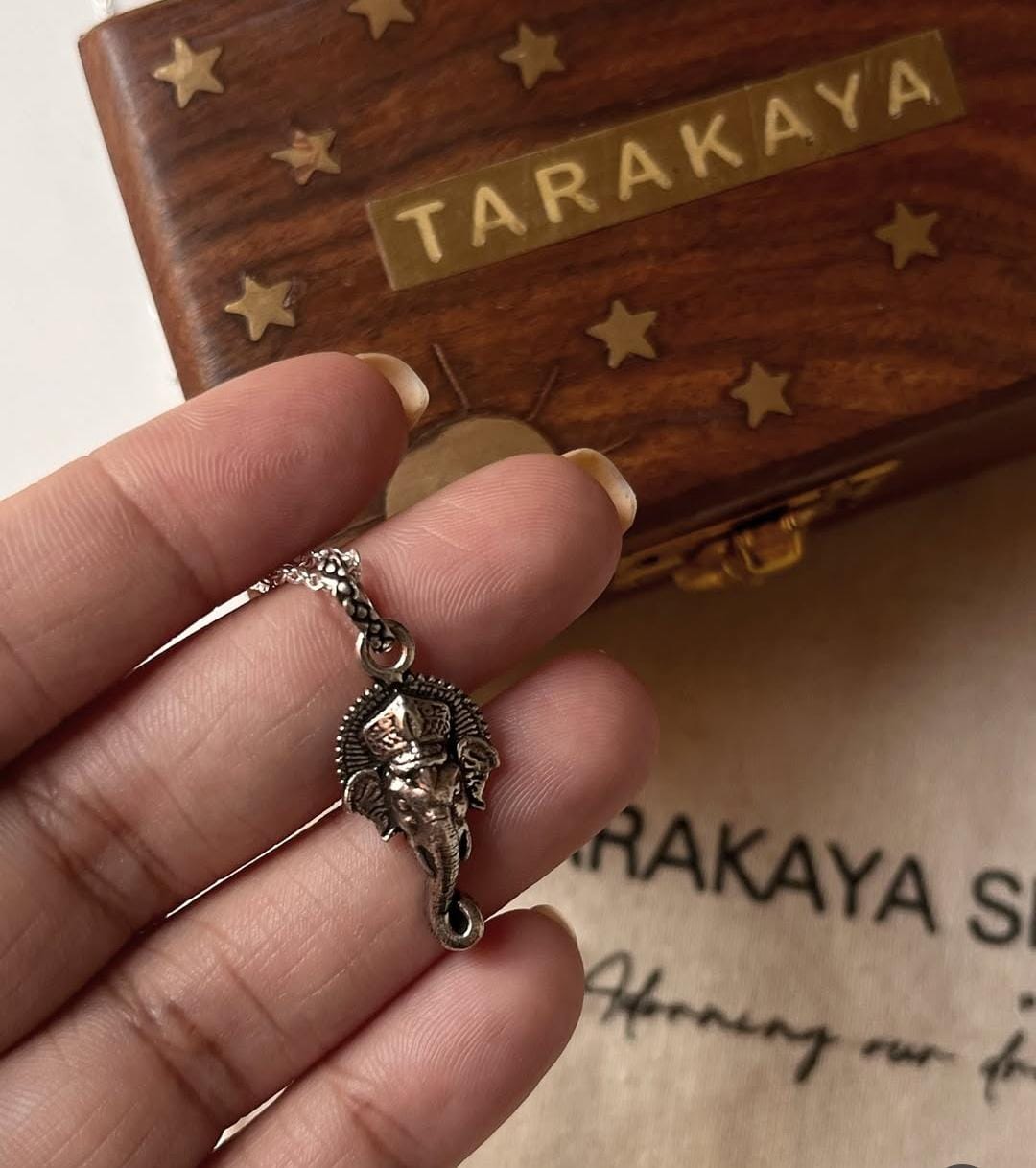 Hand holding a Ganesha face big silver pendant, pure silver 925, with a decorative wooden box in the background.