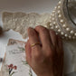 Gold vermeil thin link stack band ring worn on a hand, surrounded by lace and pearls.