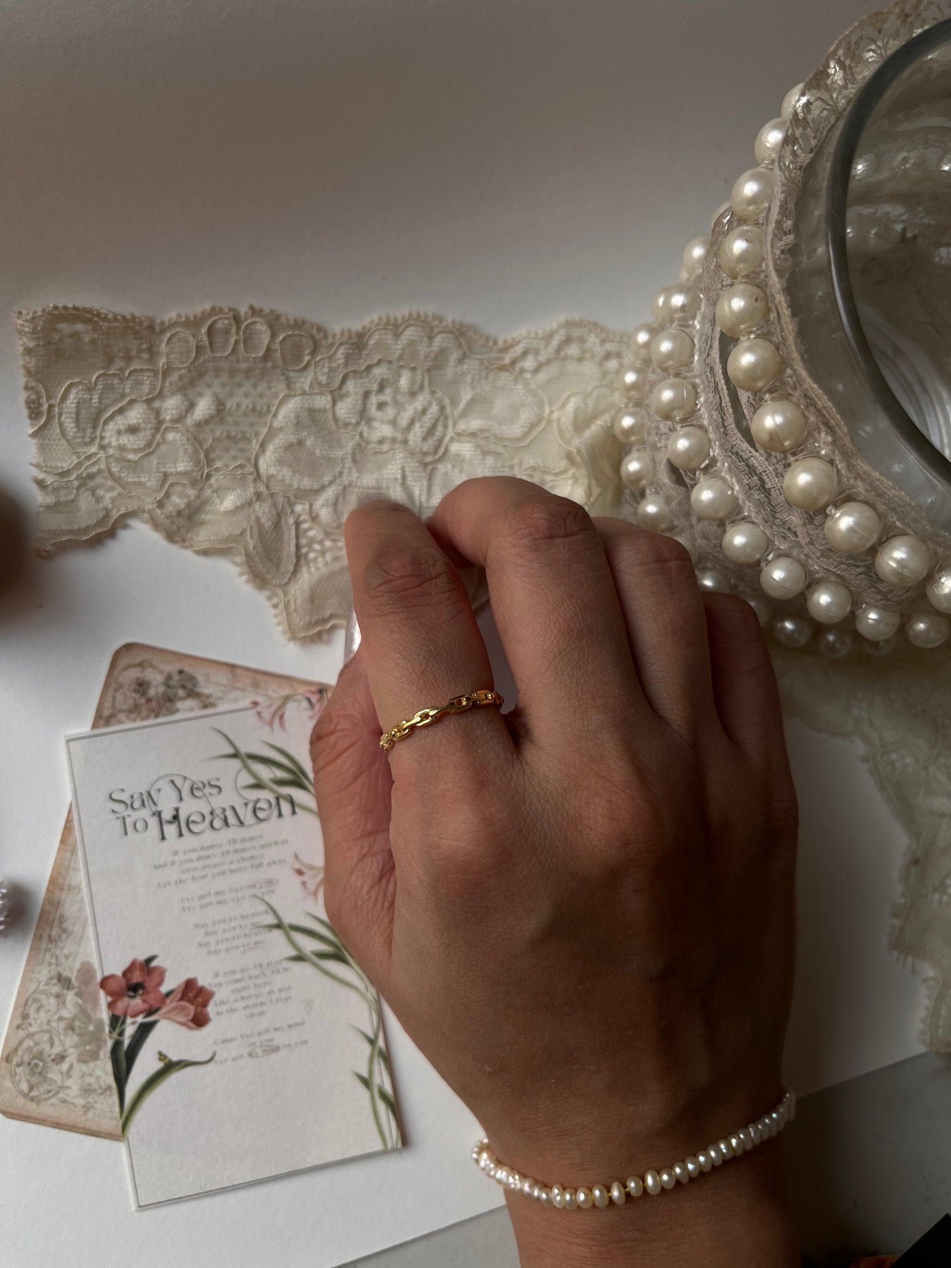 Gold vermeil thin link stack band ring worn on a hand, surrounded by lace and pearls.