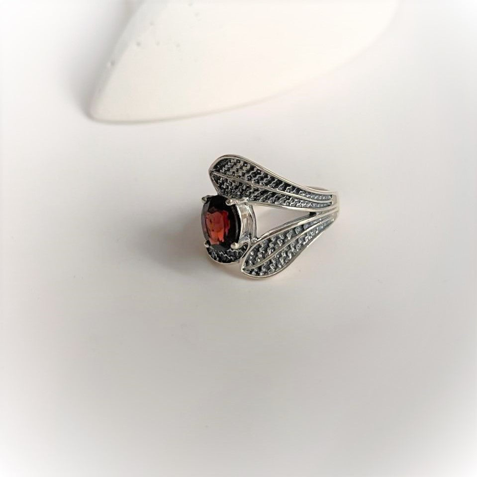 Silver ring with a garnet centerpiece and leaf wrap design