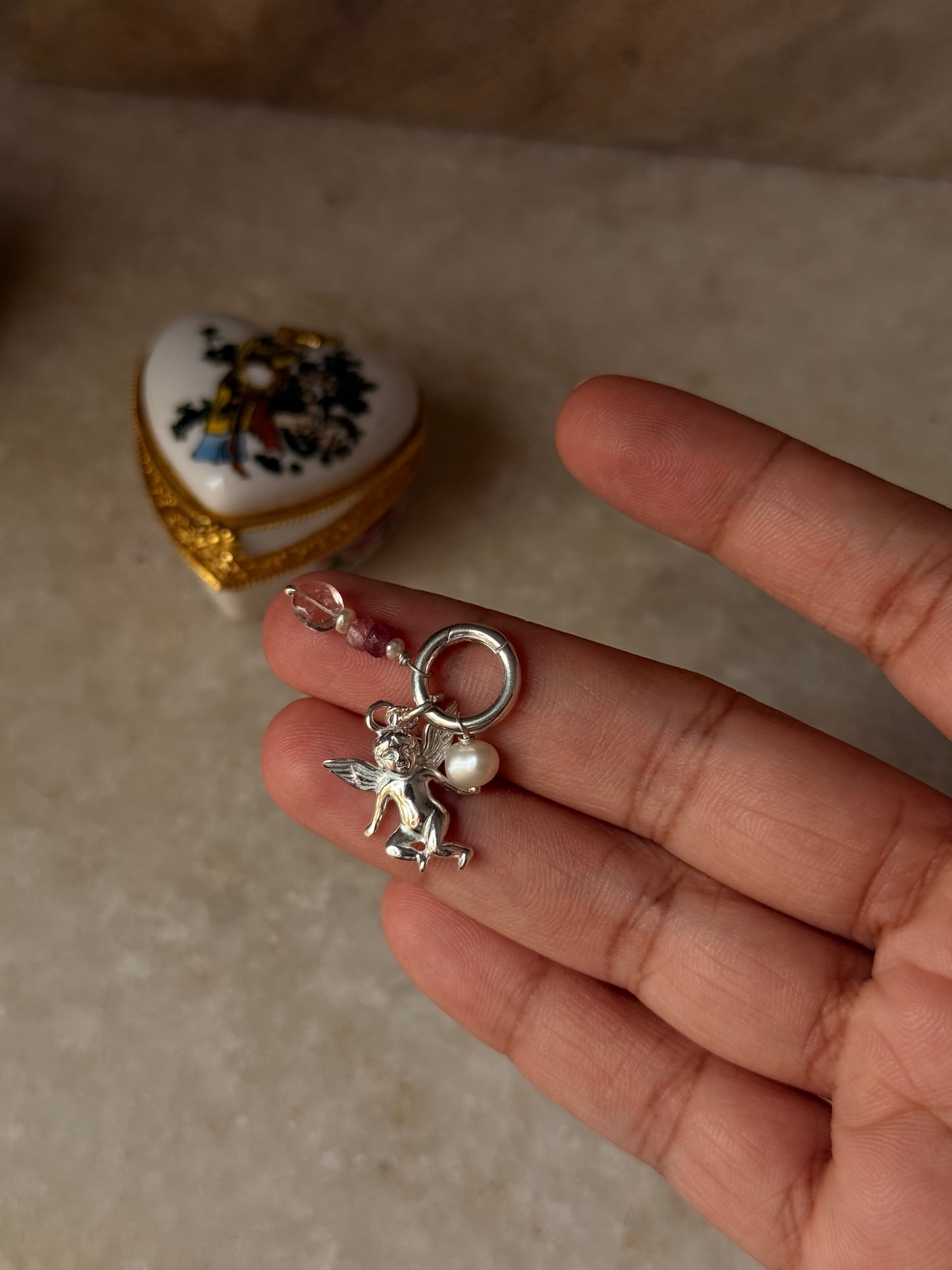 925 Sterling Silver Cherub Angel charm with Clear Quartz heart and Pearl charm in hand on marble surface.