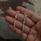 Hand holding 925 Sterling Silver handcrafted tribal contemporary Mandali earrings on textured surface.