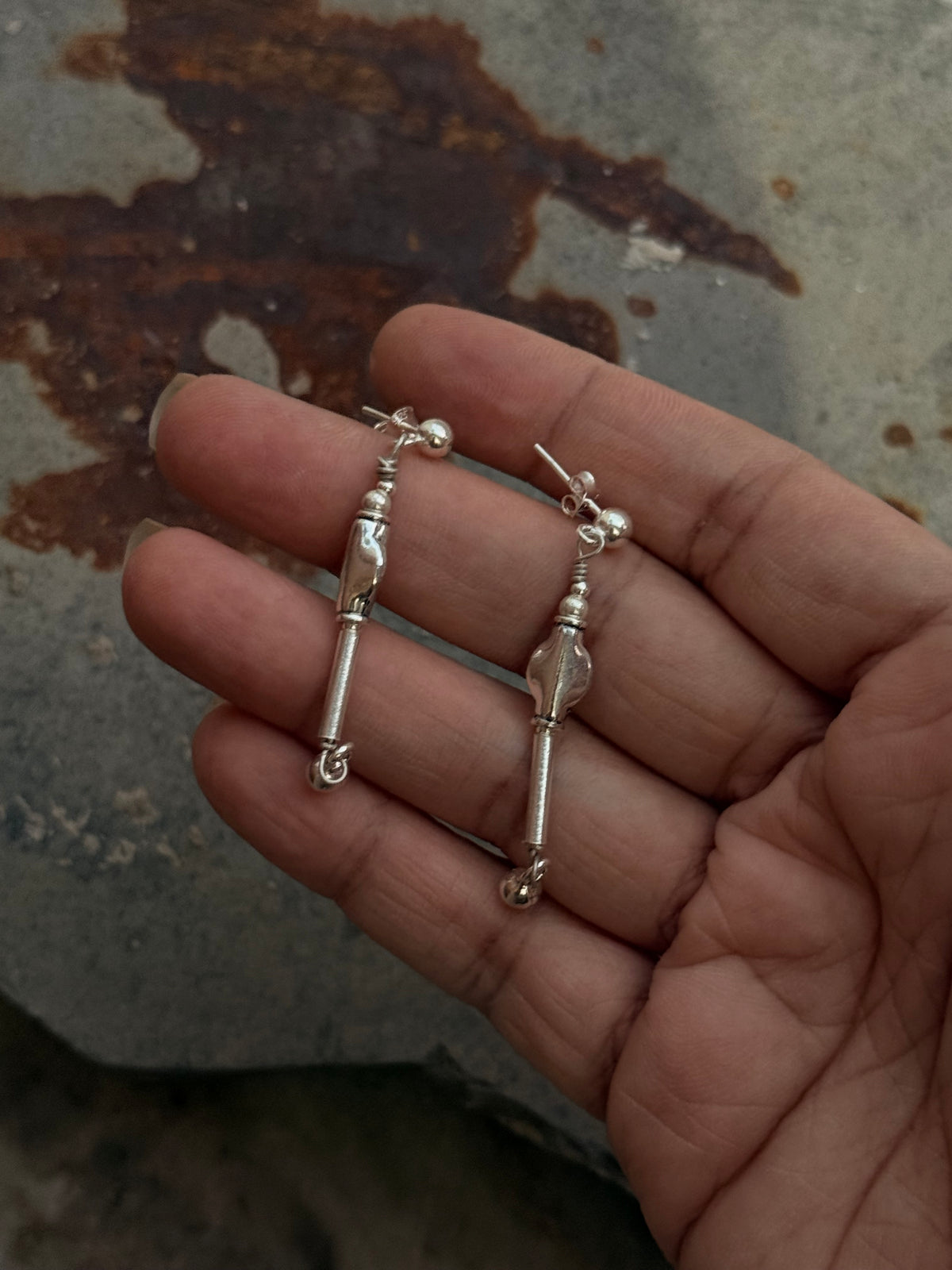 Hand holding 925 Sterling Silver handcrafted tribal contemporary Mandali earrings on textured surface.