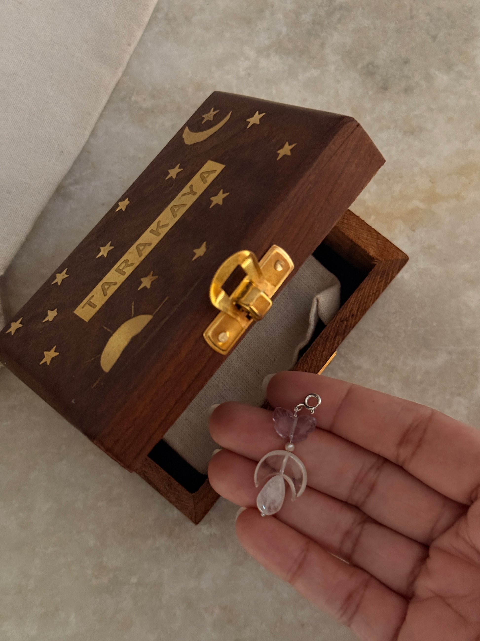 Hand holding 925 Sterling Silver Amethyst, Clear Quartz Moon & Moonstone Charms beside a decorative wooden box.