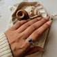 Hand wearing a Black Onyx Rawa Tribal Silver Ring on a marble surface, with decorative shells nearby.
