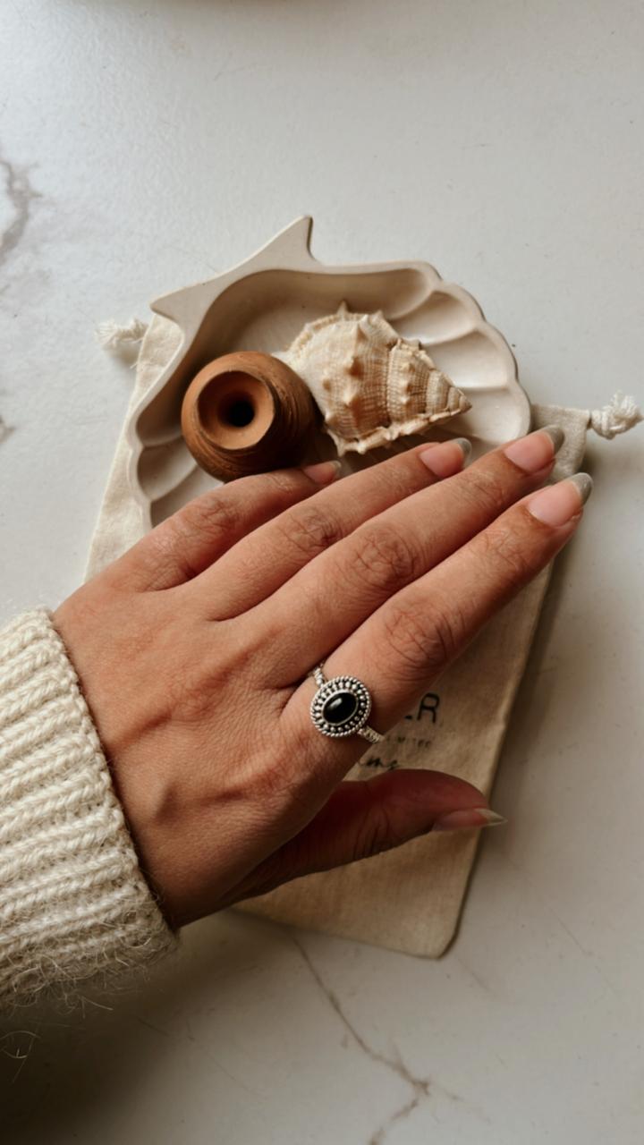 Hand wearing a Black Onyx Rawa Tribal Silver Ring on a marble surface, with decorative shells nearby.
