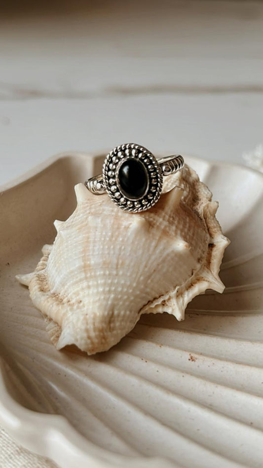 Black Onyx Rawa Tribal Silver Ring on a seashell, showcasing its deep black color and intricate silver detailing.