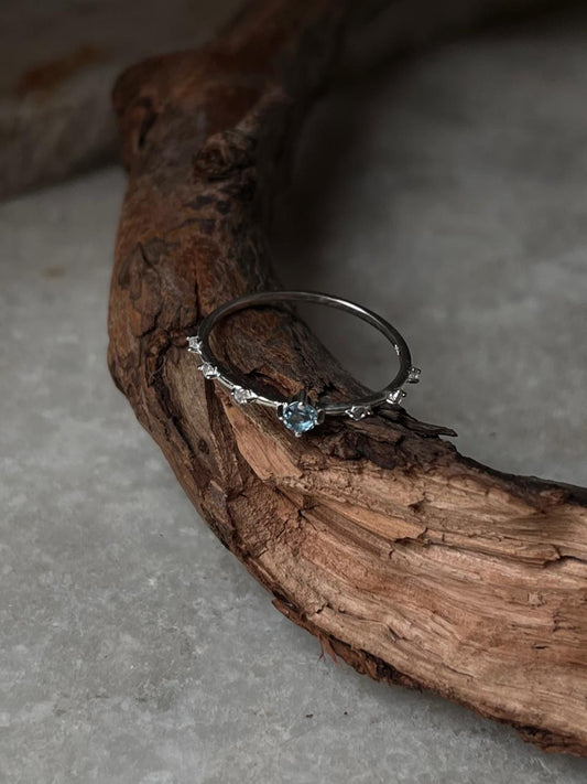 Blue Topaz & White Topaz dainty band ring on natural wood background, crafted in 925 sterling silver.
