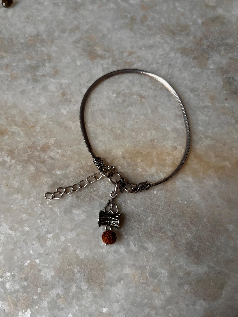 Flat Snake Antique & Trishul Damru Rakhi with Rudraksh and 925 sterling silver charm on marble background.