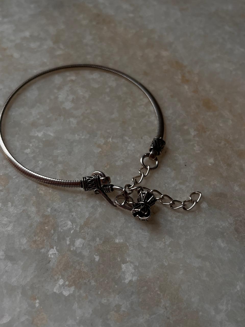 Flat snake patterned silver rakhi with small Shiva Damru  