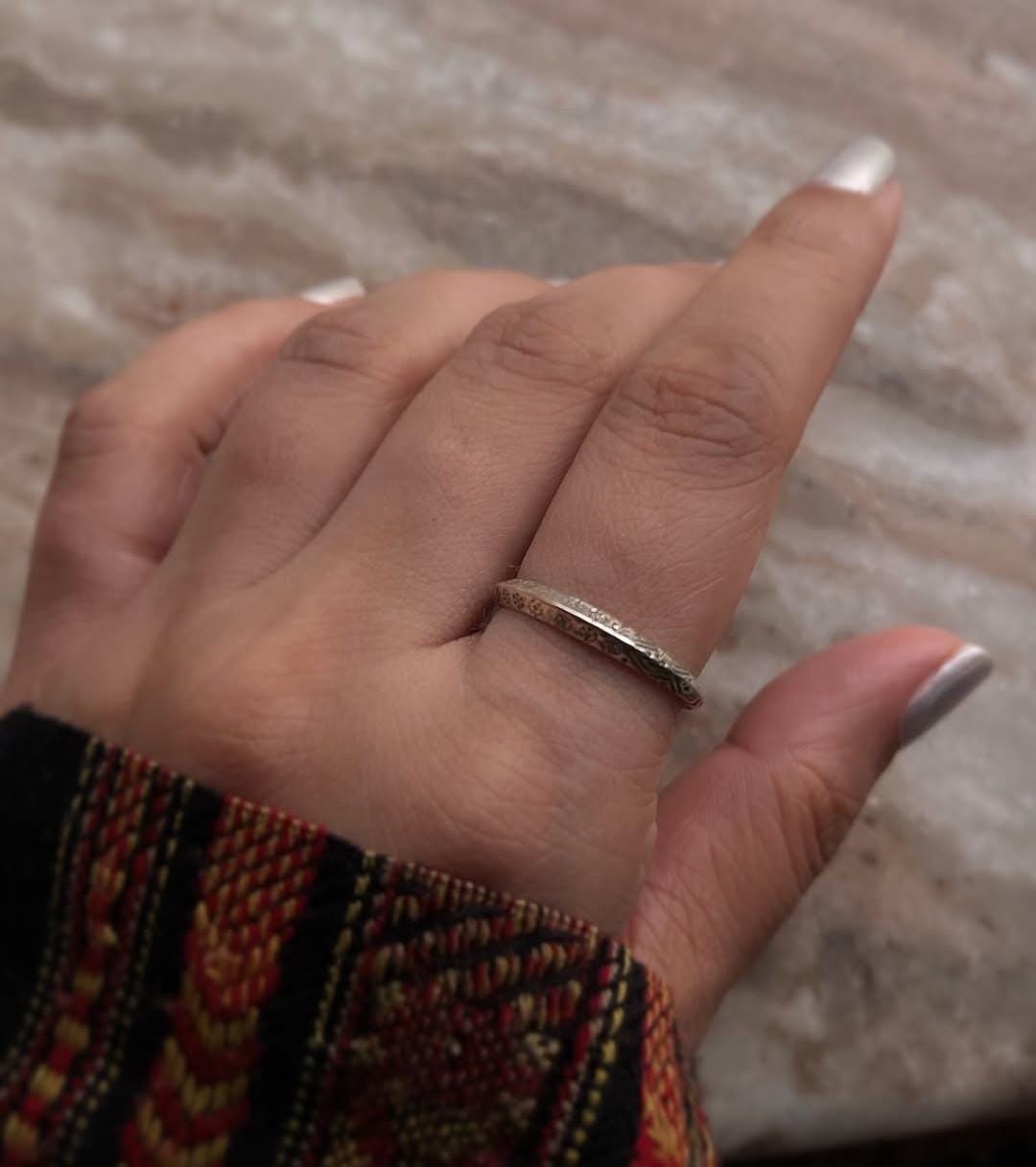 Hand wearing a Tribal Edge 925 Silver Ring, showcasing its unique design and shine on a textured surface.