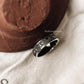 Intricately designed Sacred Journey 925 silver ring alongside a decorative pot on a soft fabric background.