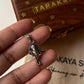 Hand holding a Ganesha face silver pendant, showcasing detailed craftsmanship and design against a decorative background.
