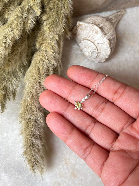 Hand holding a Tribal Tiny Peridot 925 Sterling Silver Necklace with natural decor in the background.